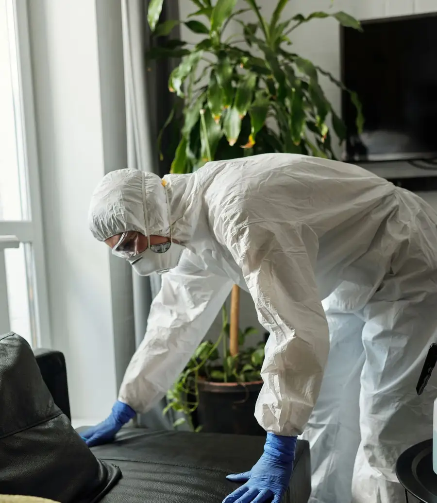 Cleanup technician in a protective suit working over a sofa