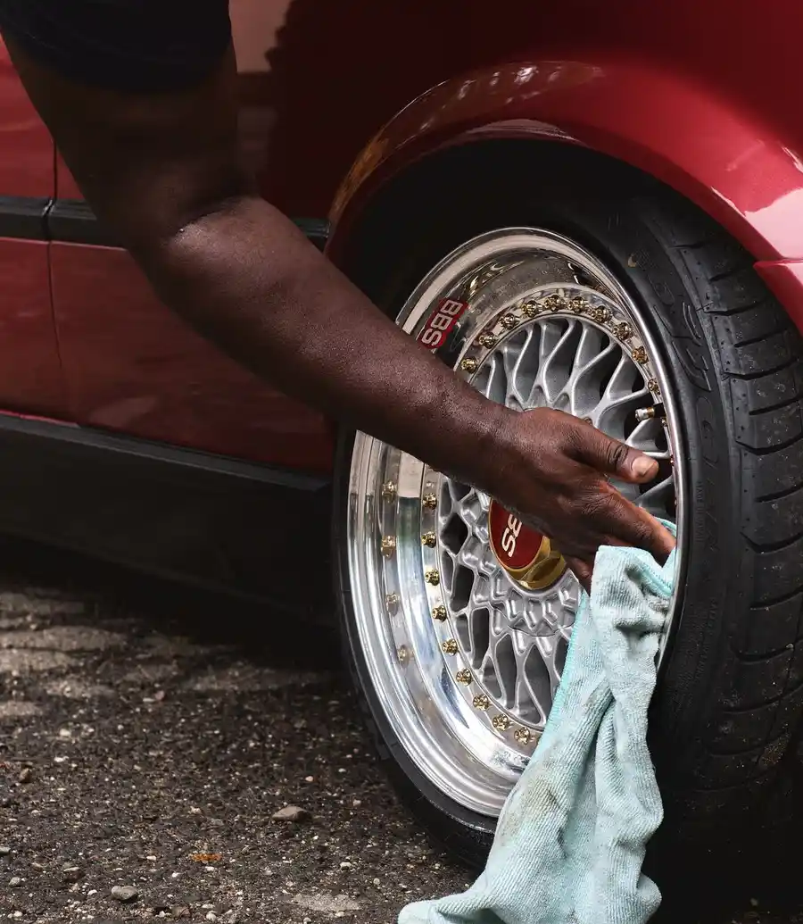 Detailer wiping down a car wheel with a cloth during a daytime detail
