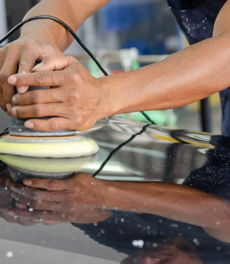 Close-up of hands polishing a car hood with a buffer in a workshop