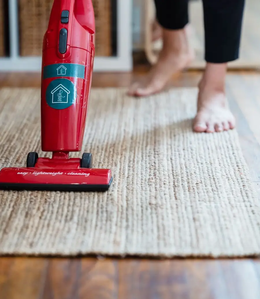 A red upright vacuum standing on a woven rug in a home
