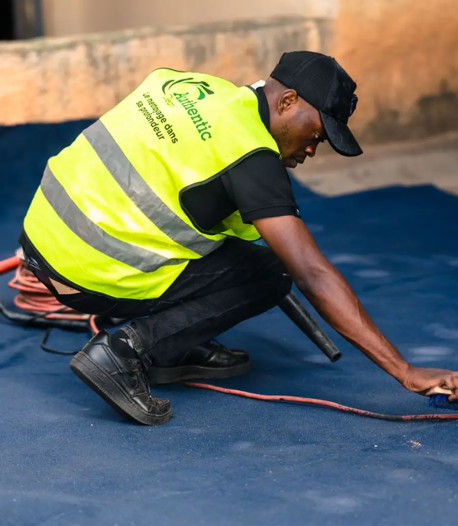 Carpet cleaner in a hi-vis vest brushing a large blue carpet