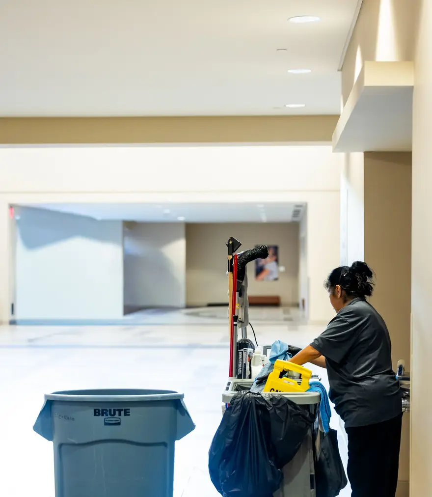 Cleaner with a supplies cart in a quiet building hallway in the evening