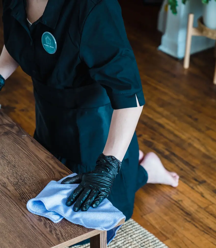 Gloved cleaner wiping a wooden table with a microfibre cloth