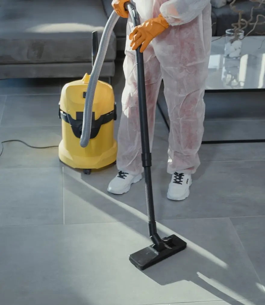 Professional cleaner in a protective suit vacuuming a modern living room