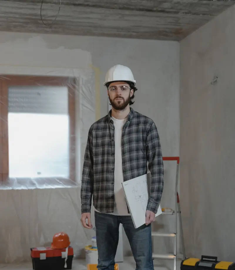 General contractor in a hard hat holding project plans in a room being renovated