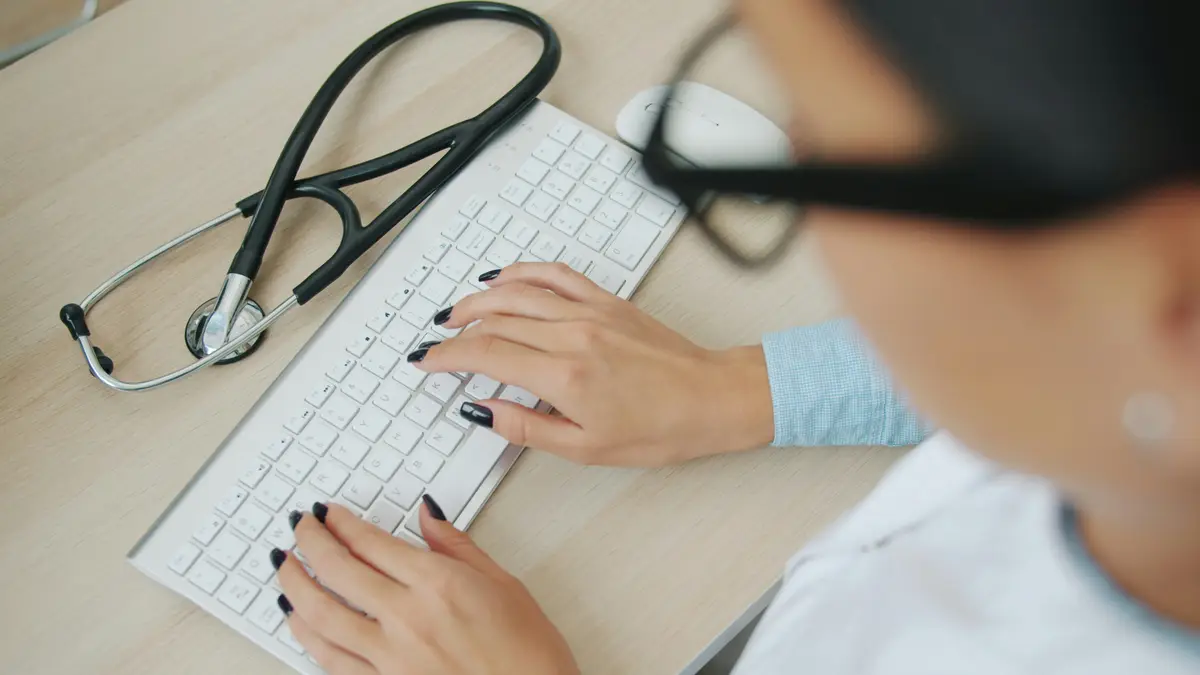 Clinician checking records at a computer, stethoscope beside the keyboard