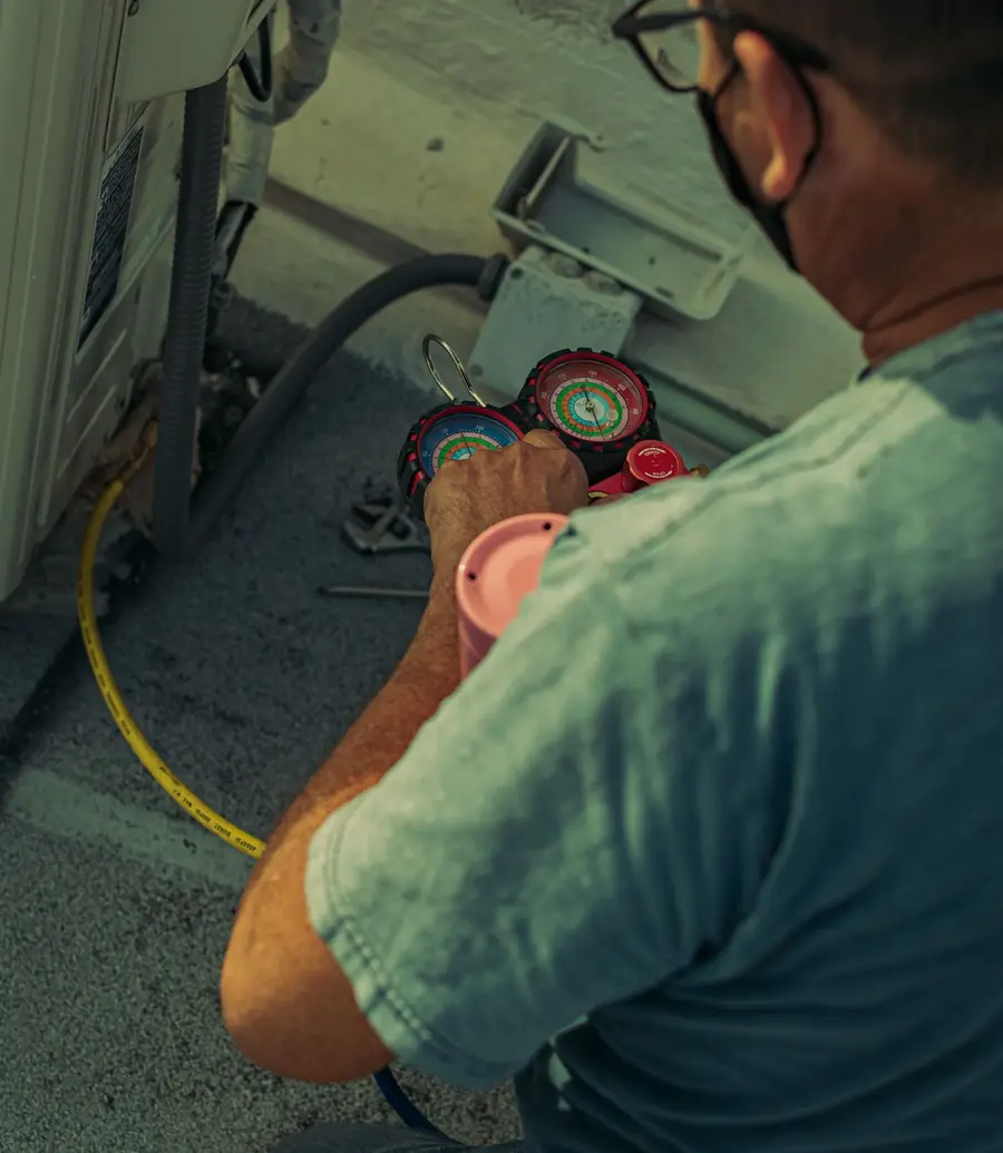 HVAC technician servicing an outdoor air conditioning unit with a manifold gauge