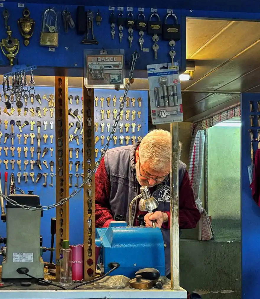 Locksmith cutting a key on a machine in a shop lined with key blanks