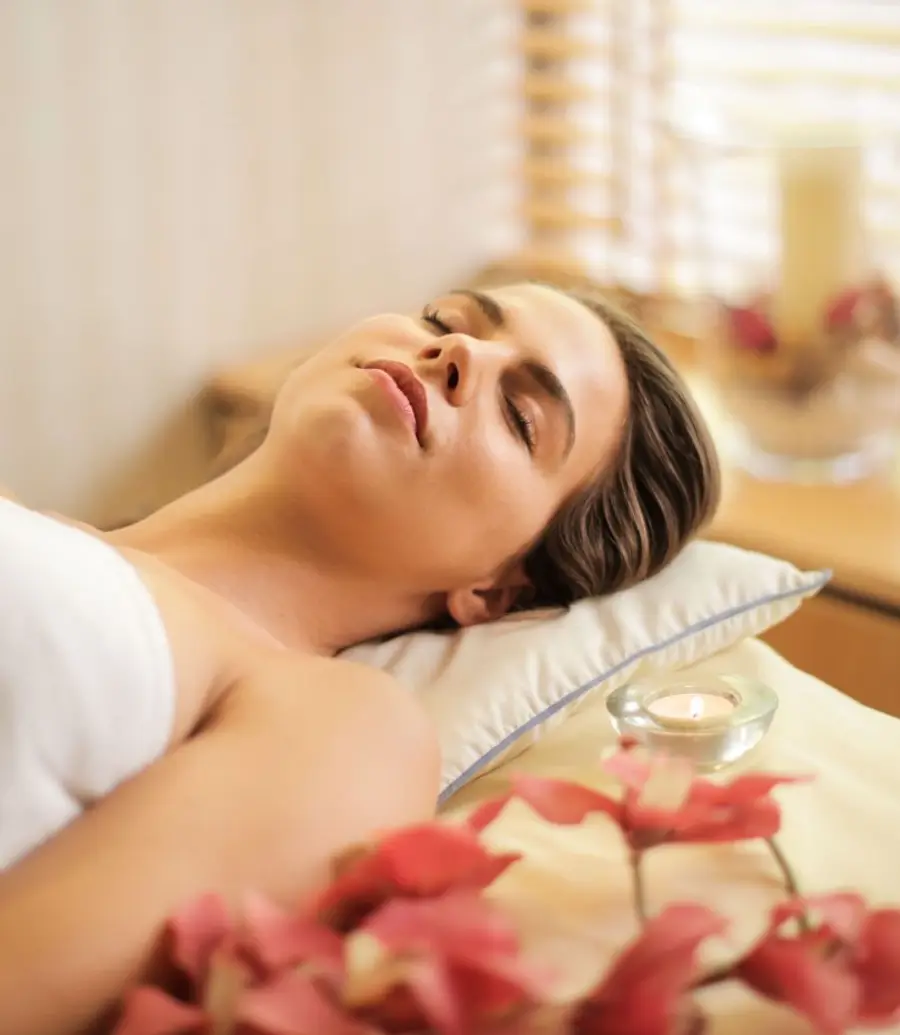A client resting peacefully on a massage table beside a candle and orchids