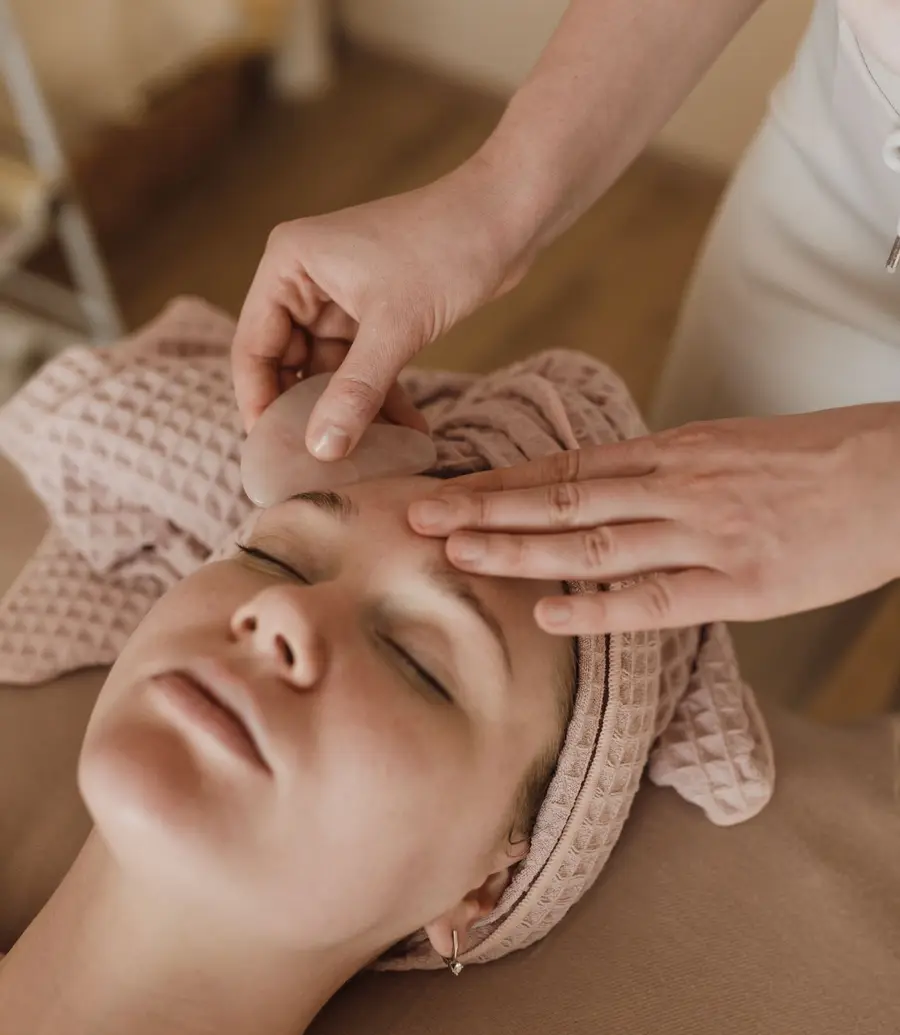 A massage therapist's hands working on a relaxed client's face in a calm treatment room