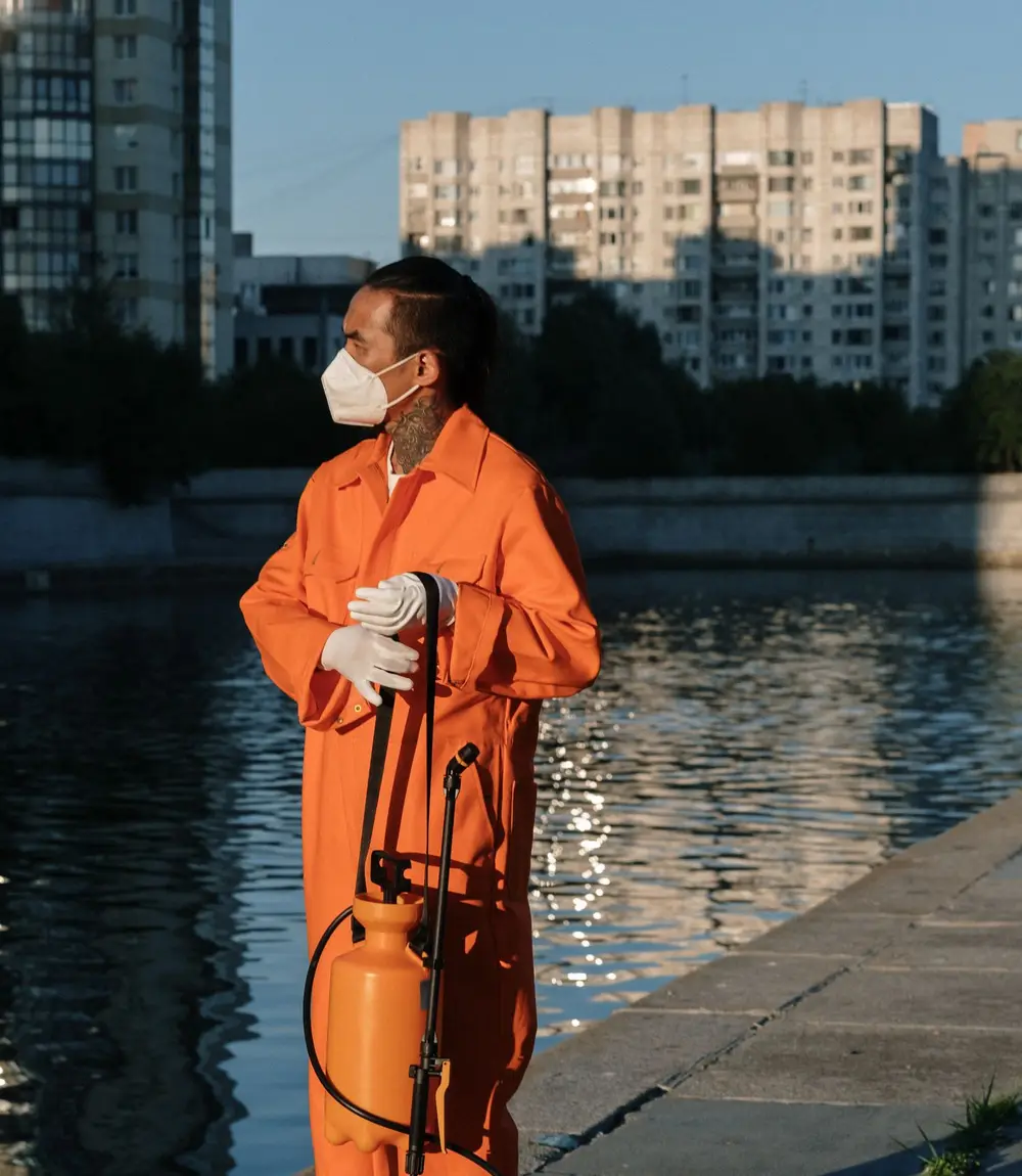 Pest control technician in coveralls at dusk holding a sprayer