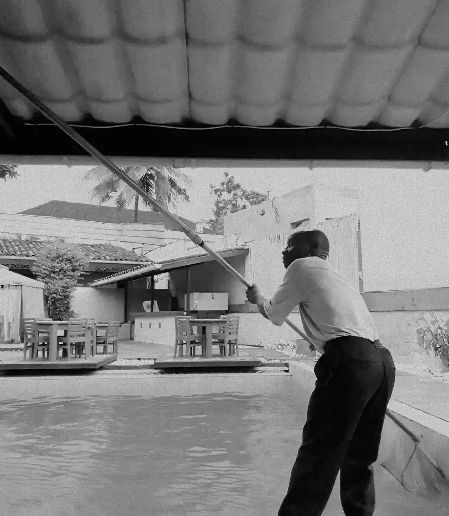 Pool technician skimming a pool with a long pole during the day
