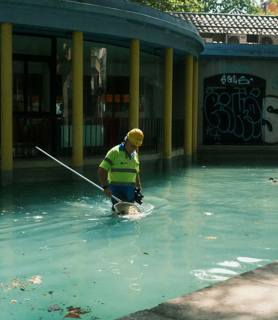 Pool technician in hi-vis clearing a green pool with a net