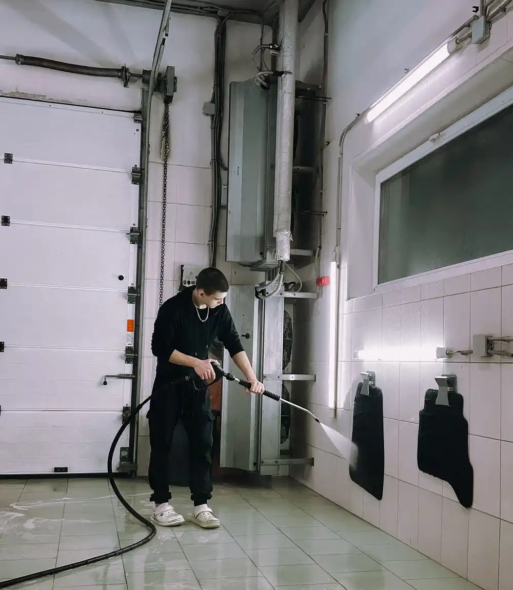 Technician pressure washing in a wash bay under artificial light at night