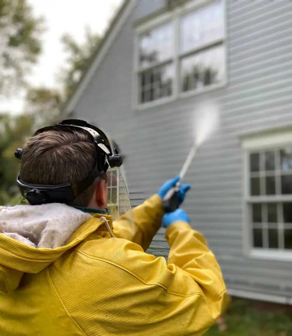Worker in yellow protective gear pressure washing the siding of a house