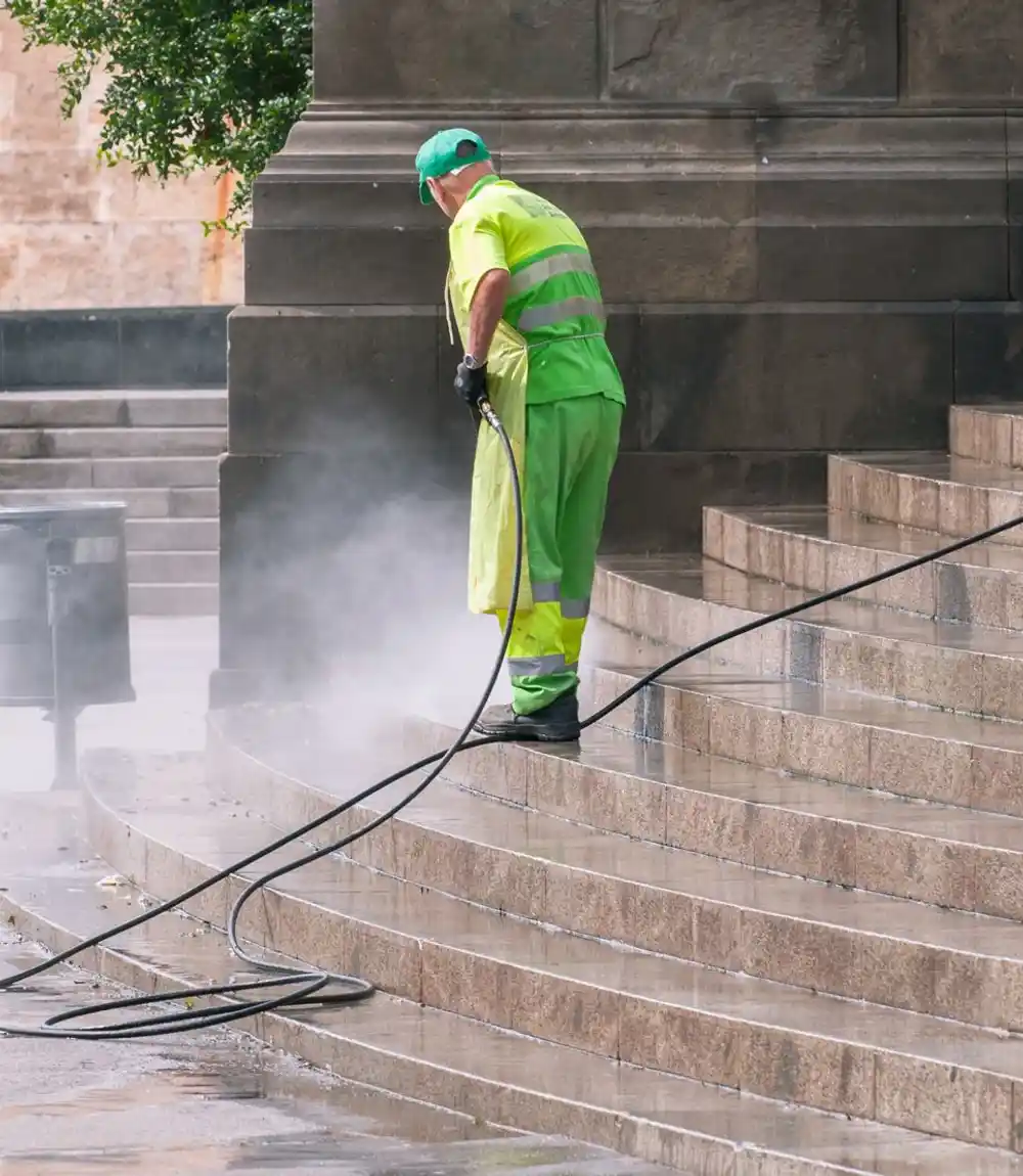 Worker in hi-vis gear pressure washing stone steps with rising steam