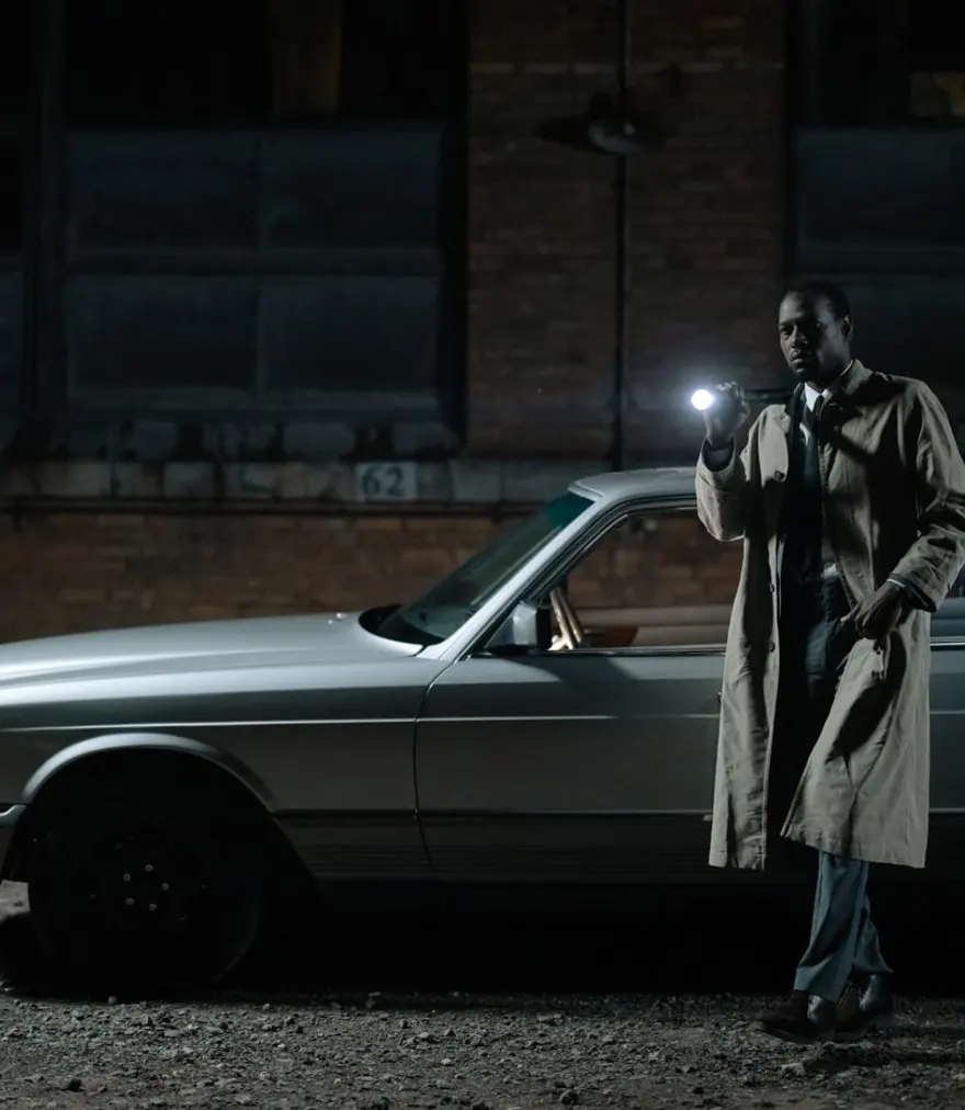 Private investigator with a flashlight beside a car at night