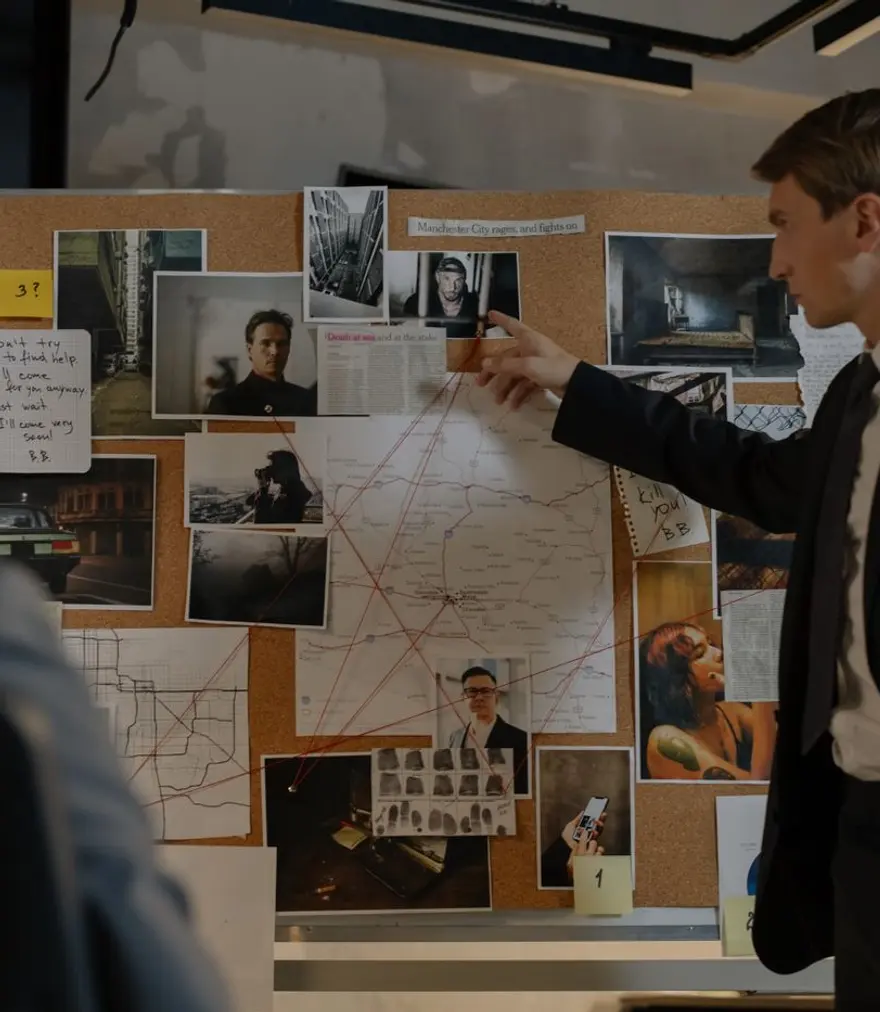 Private investigator studying photographs and a map on an evidence board