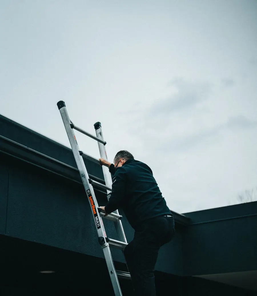 Roofing contractor climbing a ladder up to a roof in low evening light