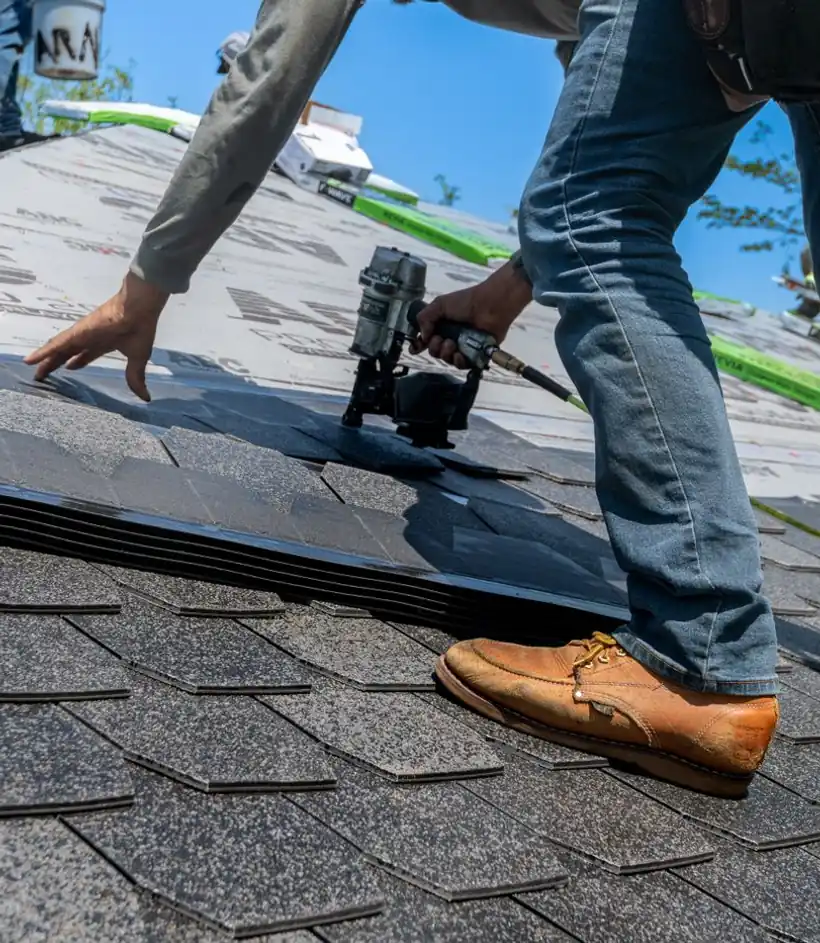 Roofer fastening asphalt shingles with a coil nail gun during a daytime job