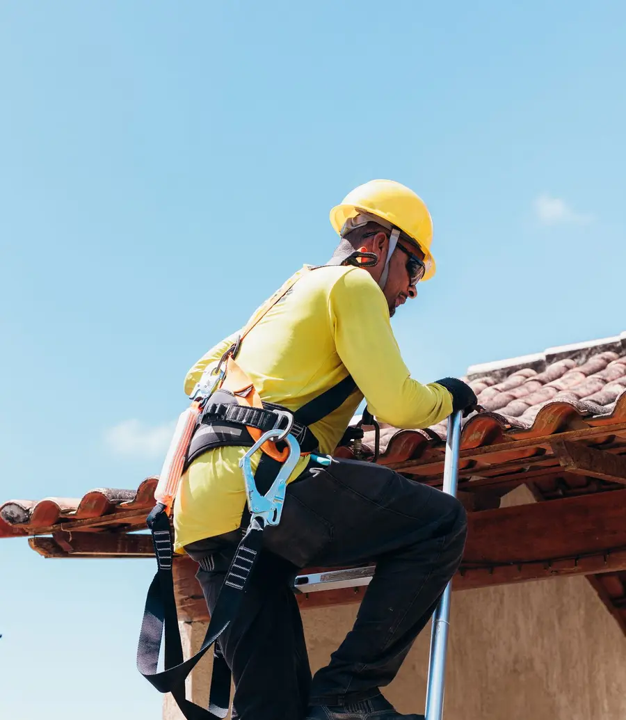 Roofer in a safety harness accessing a tiled roof from a ladder
