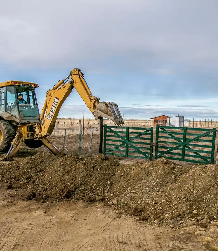 Backhoe loader digging soil at a property entrance