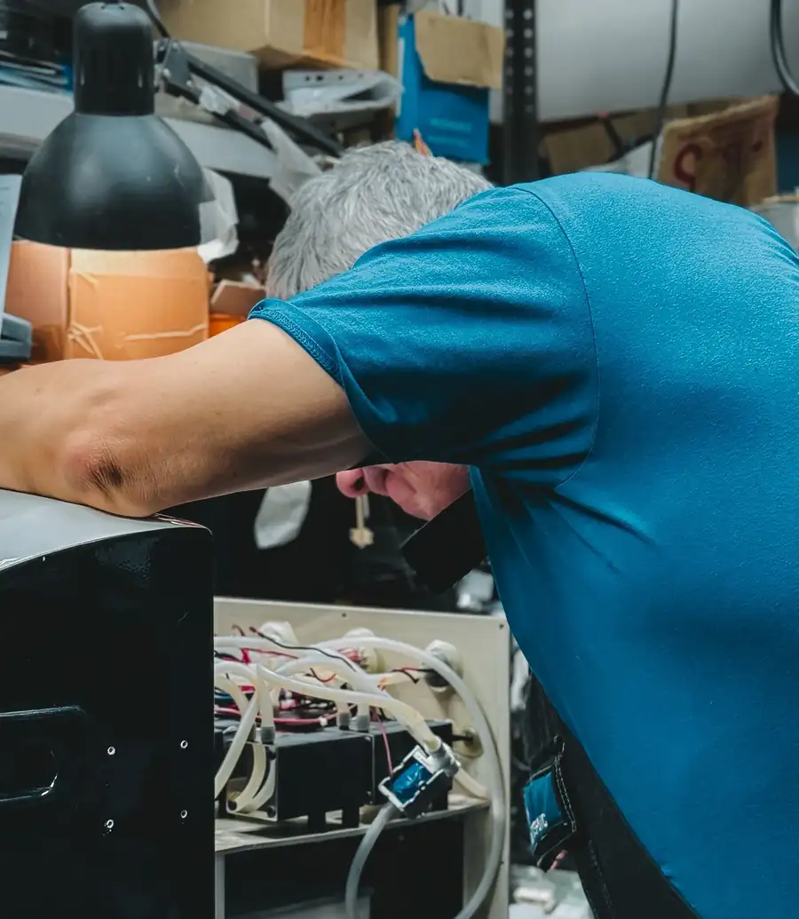 Technician bent into an appliance under a warm work lamp in a dim workshop