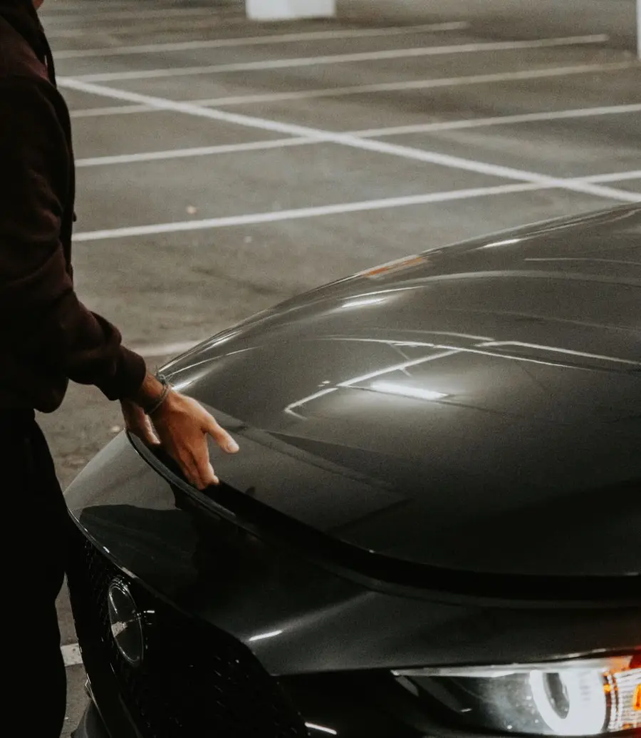 Person opening a car hood in a dimly lit parking garage at night