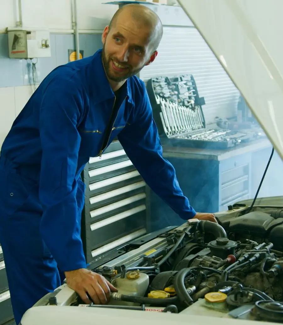Smiling mechanic in blue overalls inspecting a car engine