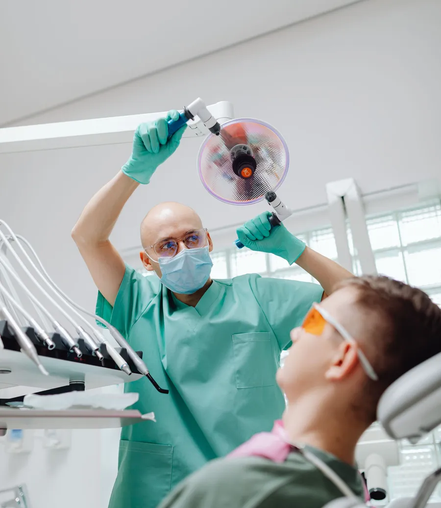 Dentist adjusting the overhead lamp above a patient wearing safety glasses