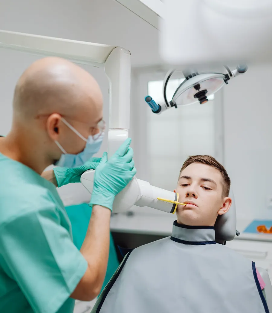 Dentist positioning an X-ray arm beside a young patient in a lead apron