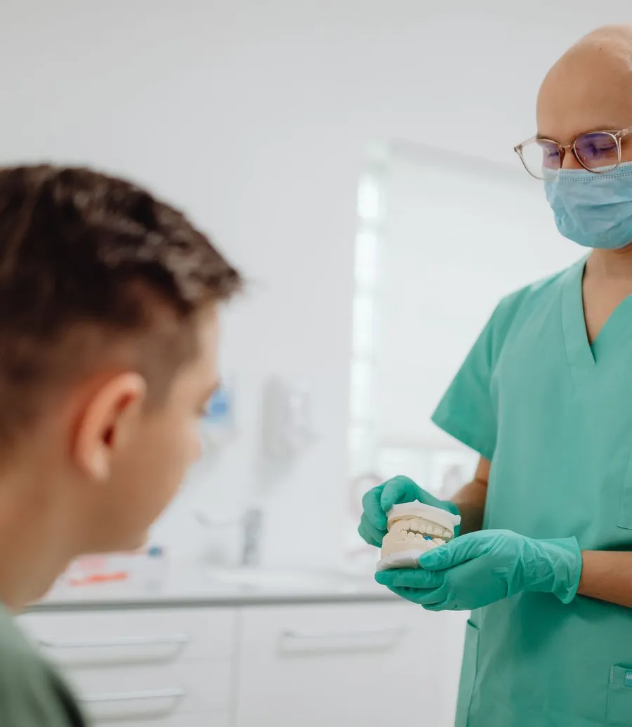 Dentist in scrubs showing a dental model to a young patient