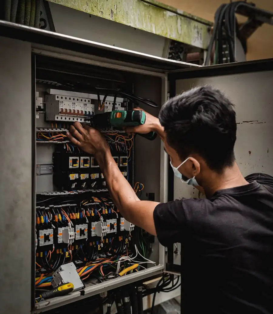 Technician drilling into an electrical panel in a dimly lit setting