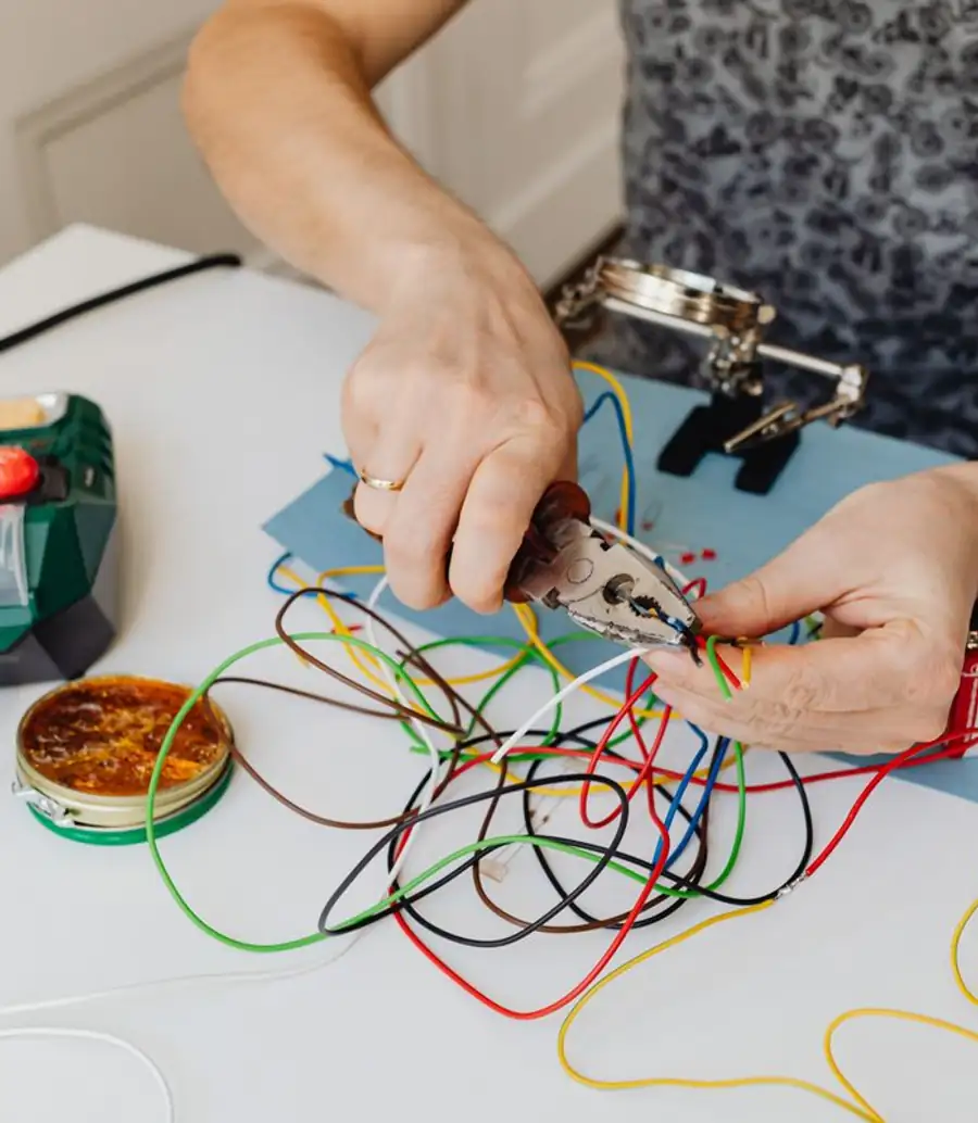 Hands stripping colored electrical wires on a workbench