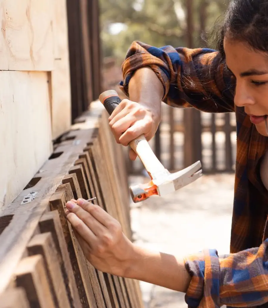 Carpenter fixing a wooden fence with a hammer during the day