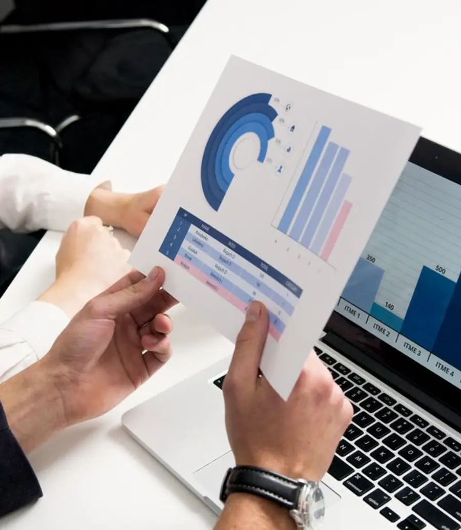 Two people reviewing financial charts on a laptop and a printed report