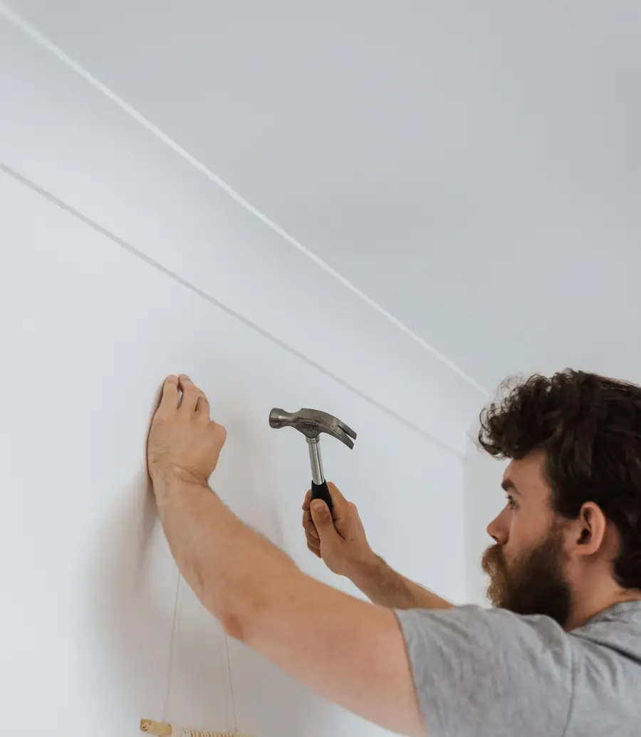 Handyman driving a fixing into a wall with a hammer during a daytime visit