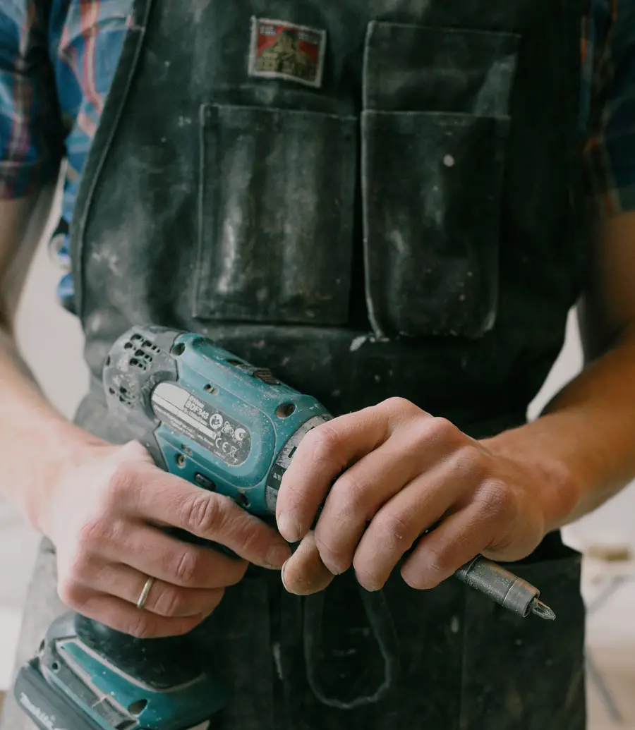 Close-up of a handyman holding a cordless drill in a work apron