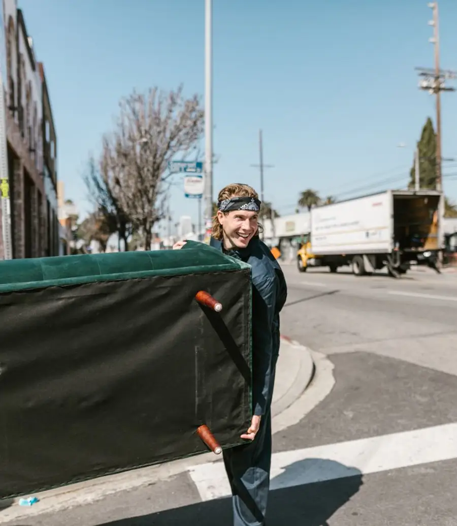 A man carrying a large couch across an urban street