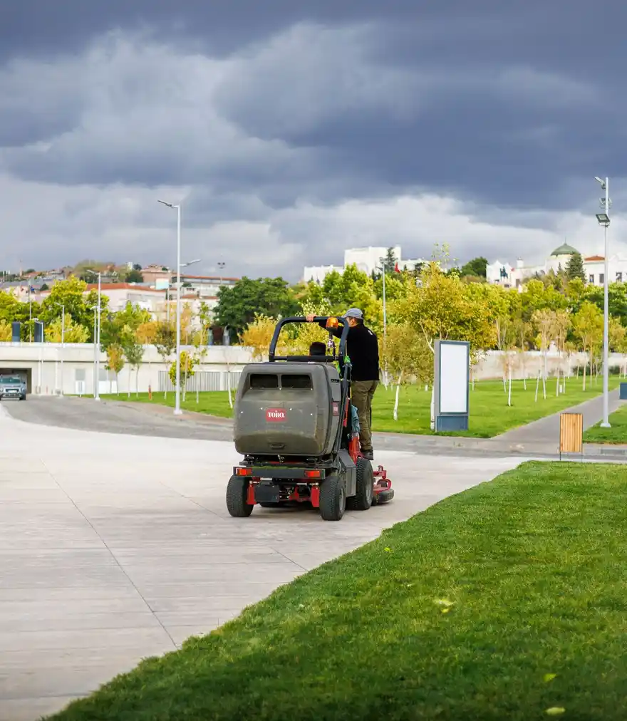 Landscaper operating a ride-on mower under an overcast evening sky