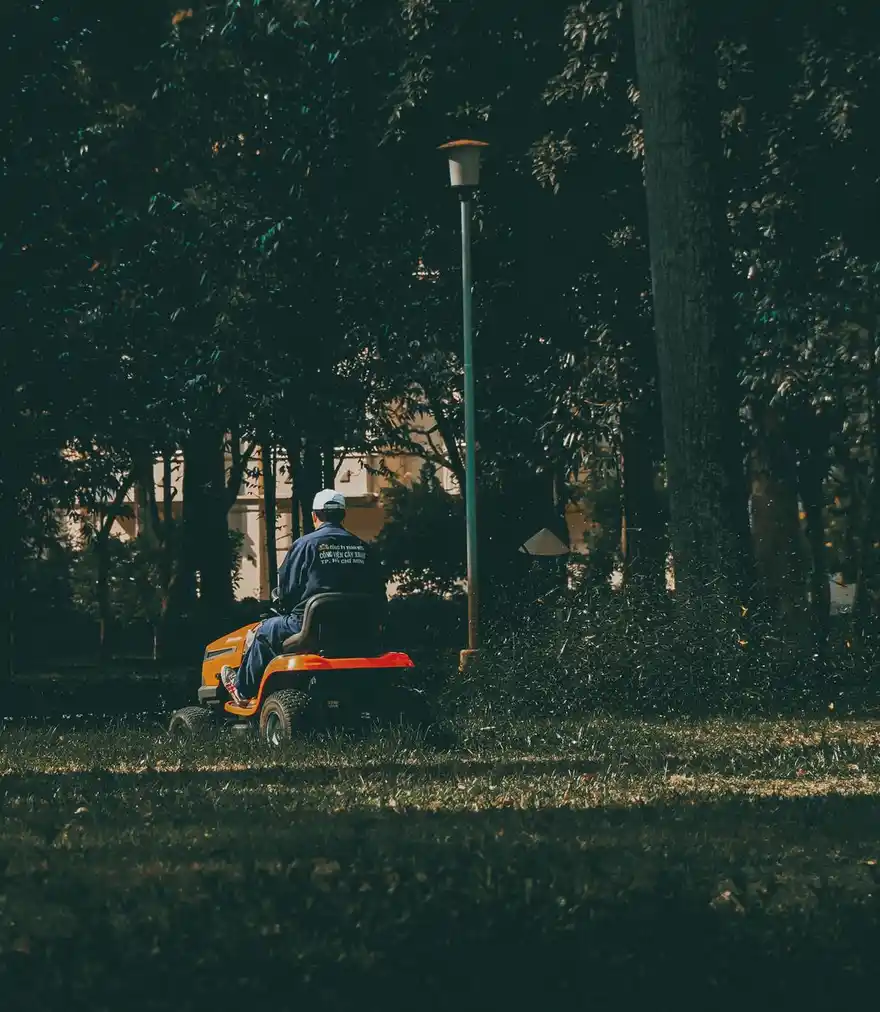 Landscaper mowing a lush green park lawn during the day