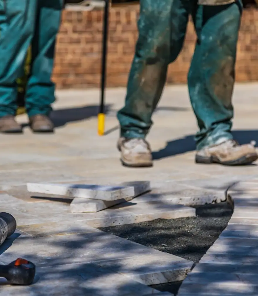 Two landscapers laying paving stones on a patio in daylight