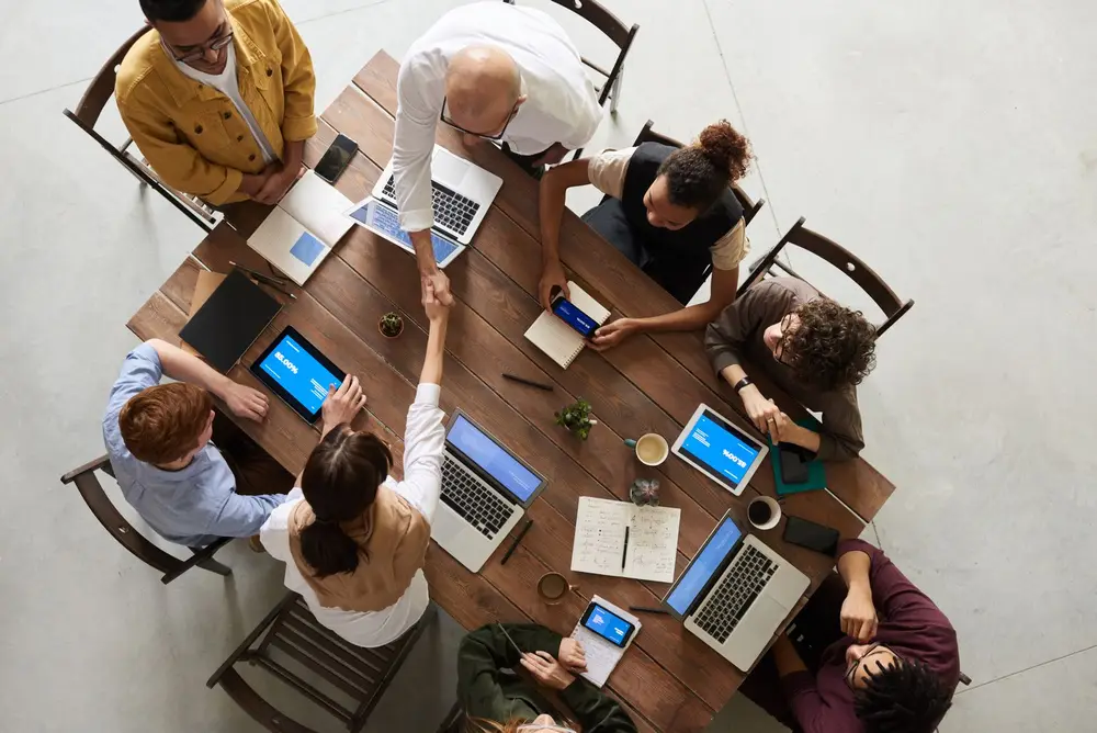Two people shaking hands across a work table to close a deal