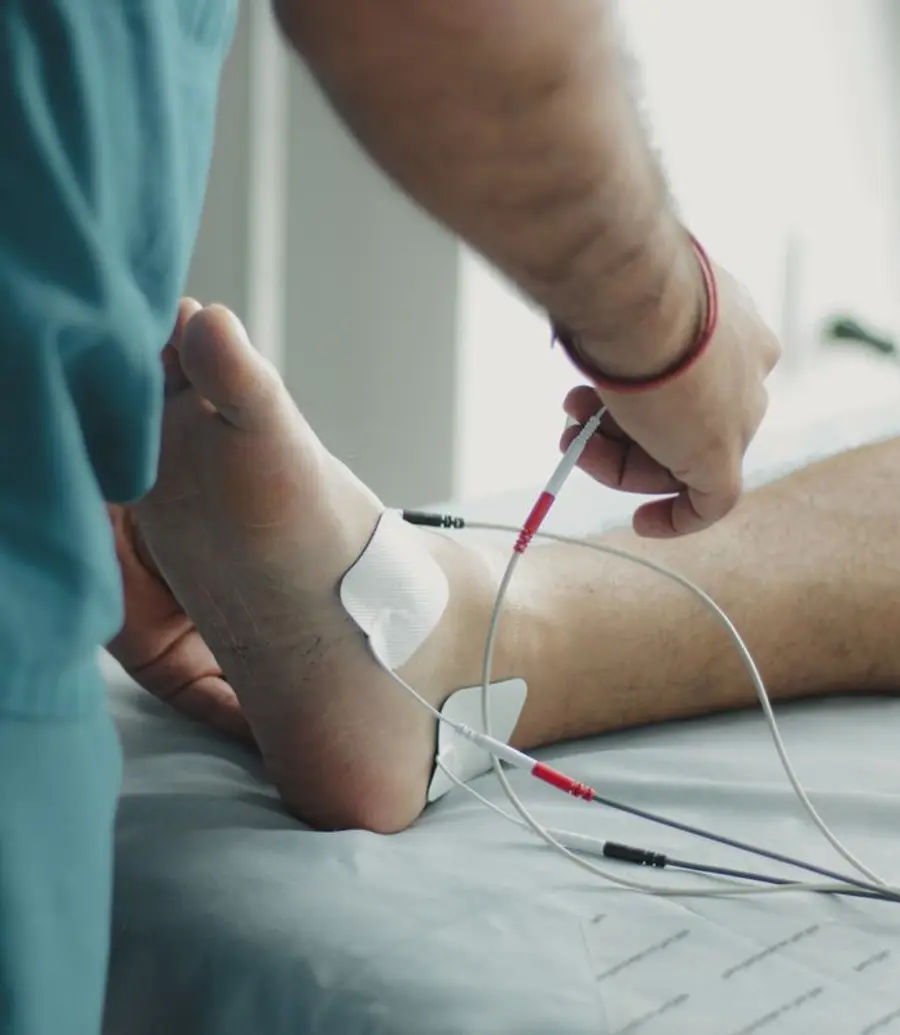 Physiotherapist applying electrode therapy to a patient leg in a dimly lit clinic
