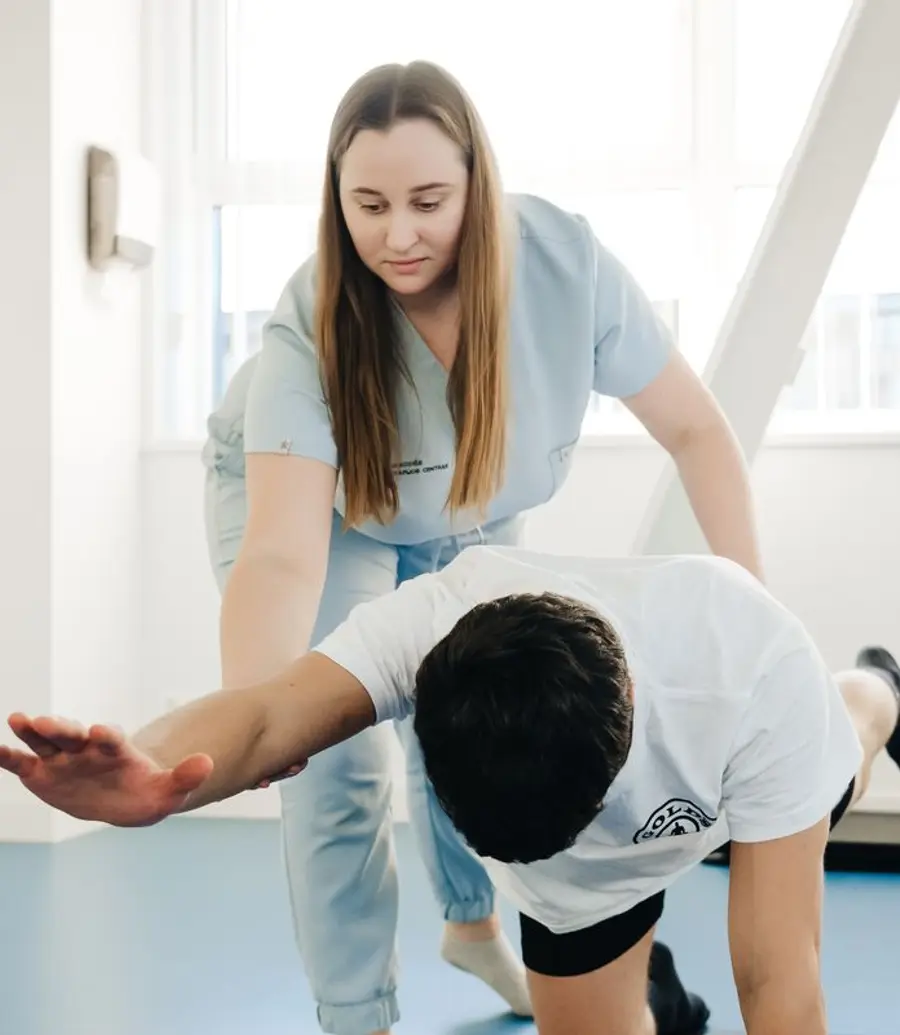 Physiotherapist coaching a patient through a floor exercise in a bright clinic
