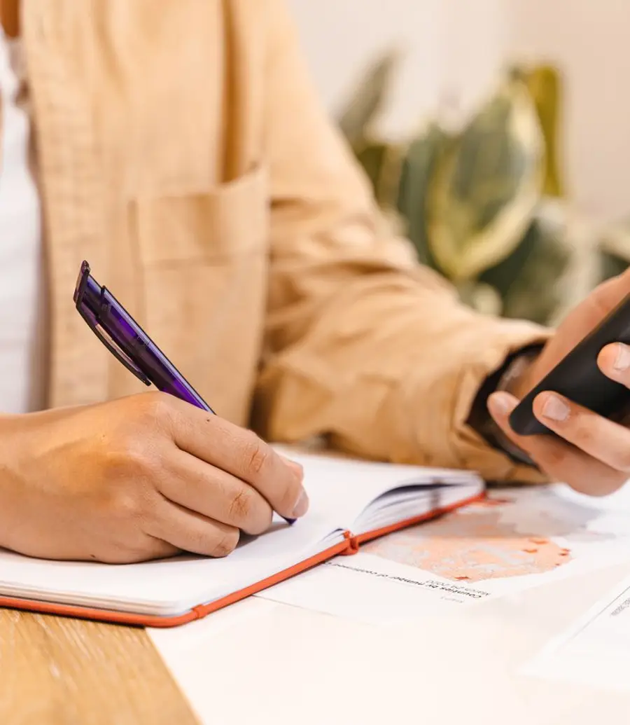 Close-up of hands holding a phone and a notebook at a desk